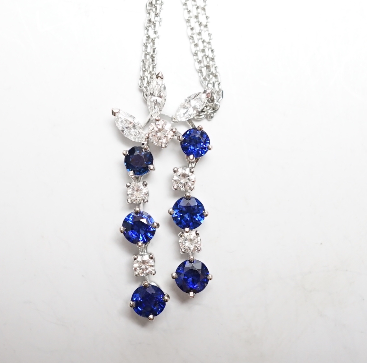 A modern 750 white metal, sapphire and diamond set cluster pendant, 31mm, on a twin strand white metal chain, 44cm, gross weight 10.3 grams, in a Bucherer box.
